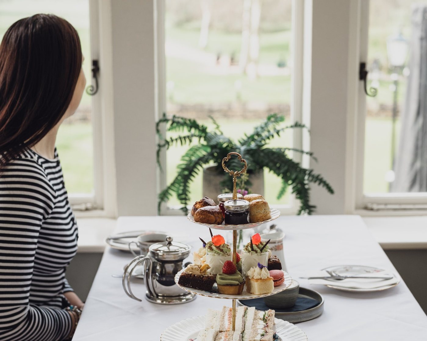 A guest at a window table looking out over the grounds, afternoon tea on the stand beside her